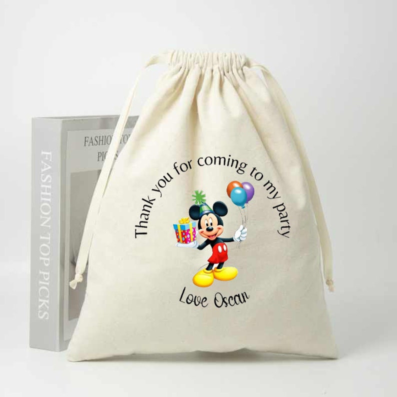 May include: A white cotton drawstring bag with a Mickey Mouse design. The bag has the text "Thank you for coming to my party" and "Love Oscan" printed on it.