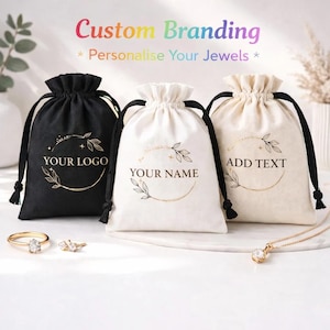 Può includere: Tre sacchetti per gioielli con coulisse in nero e bianco sporco. Ogni borsa presenta un design circolare dorato con il testo: "YOUR LOGO", "YOUR NAME" e "ADD TEXT". Le borse sono esposte con gioielli in oro, tra cui anelli e una collana.