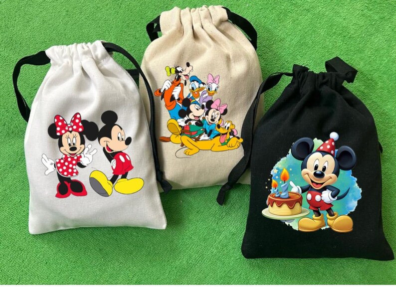 May include: Three drawstring bags with different Disney character designs. The first bag is white with Mickey Mouse and Minnie Mouse. The second bag is beige with Mickey Mouse, Minnie Mouse, Donald Duck, Goofy, and Pluto. The third bag is black with Mickey Mouse wearing a birthday hat.