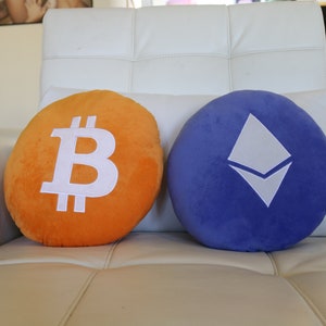 May include: Two plush pillows, one orange with a white Bitcoin symbol and one blue with a white Ethereum symbol.