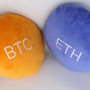 May include: Two plush pillows, one orange with the text "BTC" and one blue with the text "ETH".