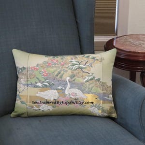 May include: Rectangular decorative pillow with a Japanese-inspired design. The pillow features a landscape with white swans, pink flowers, and gold accents. The text "SewInspiredByJapan/Etsy.com" is printed on the bottom.