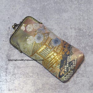 May include: A gold and pink fabric eyeglass case with a floral and geometric pattern. The case has a metal clasp.
