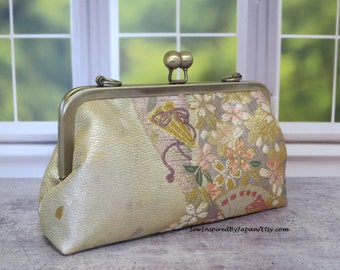 May include: A small, gold clutch purse with a floral pattern and a gold clasp. The purse is made of a fabric with a subtle sheen. The clasp has two round knobs on top.