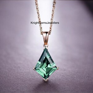 May include: A gold-colored necklace with a pendant featuring a large, square-cut, emerald-green gemstone. The pendant is suspended from a delicate chain. The text "KnightGemsJewellers" is visible.