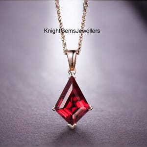 May include: A rose gold necklace featuring a kite-shaped, deep red gemstone pendant suspended from a delicate chain. The text KnightGemsJewellers is visible above the pendant. The design includes a four-prong setting holding the faceted stone.