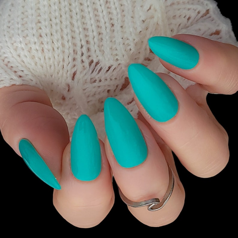 May include: Close-up of a hand with five turquoise almond-shaped nails. The nails are painted a bright turquoise color and have a matte finish.
