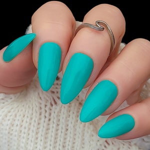 May include: Close-up of a hand with five turquoise-colored almond-shaped nails. The nails are long and have a glossy finish.
