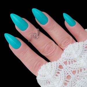 May include: A hand with turquoise nail polish and a silver wave ring. The hand is wearing a white crocheted fingerless glove.