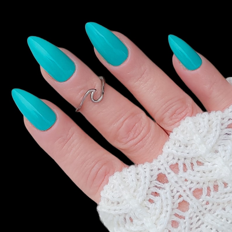 May include: A hand with turquoise nail polish and a silver wave ring. The hand is wearing a white crocheted fingerless glove.