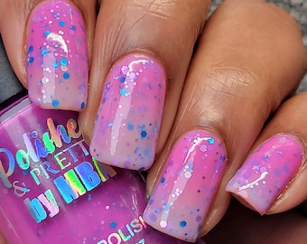 May include: A close-up of a hand with pink and white ombre nail polish with iridescent glitter. The bottle of nail polish is labeled "Polish & Pretty by MHB" and "Nail Polish 15ml .50oz".