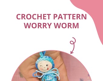 May include: A crocheted worry worm with a blue and white striped body and a wooden head with a smiling face. The worm is being held in a hand.