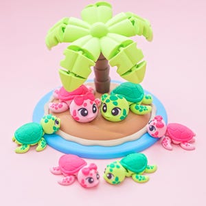 May include: A collection of colorful polymer clay turtle figurines and a palm tree on a small island. The turtles are green and pink with cute faces. The palm tree is light green and brown, set against a pink background.