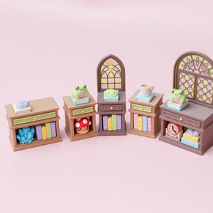 May include: A collection of five miniature brown wooden furniture pieces including cabinets and shelves. The pieces are decorated with small figurines of frogs, a mushroom, a clock, books, a crystal, and a cup, with two pieces featuring stained glass.