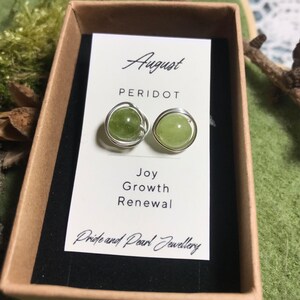 May include: Peridot stud earrings in a brown box. The earrings are round, light green gemstones wrapped in silver wire. The card inside the box reads "August PERIDOT Joy Growth Renewal" and "Pride and Pearl Jewellery".
