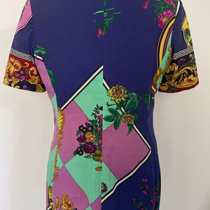 May include: A short-sleeved blazer with a vibrant, patterned design. The blazer features a color block design with purple, green, and blue panels. Floral and gold accents adorn the sleeves and collar, creating a bold, eye-catching look.