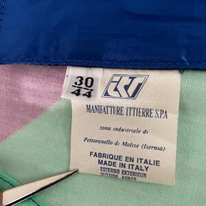 May include: A close-up of a garment tag with the text "MANIFATTURE ITTIERRE S.P.A." and "FABRIQUE EN ITALIE MADE IN ITALY". The tag also shows the size "30/44". The garment has a colorful patchwork design.