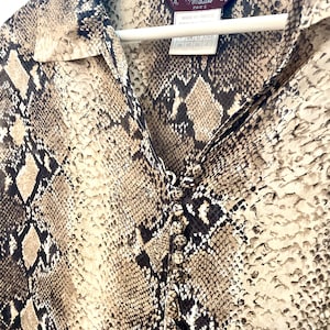 Könnte beinhalten: Ein braunes und schwarzes Hemd mit Schlangenhautmuster und Kragen. Das Hemd hat ein Etikett mit der Aufschrift "John Galliano Paris" und "Made in France".