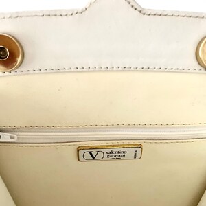 Pode incluir: O interior de uma bolsa de m&atilde;o de couro branco com um z&iacute;per dourado e uma etiqueta dourada Valentino Garavani.