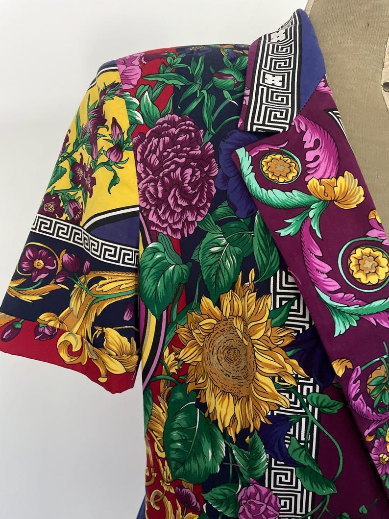 May include: A colorful blazer with a vibrant floral pattern featuring sunflowers, peonies, and other flowers in shades of yellow, purple, and red. The blazer has a unique design with a mix of patterns and colors, perfect for a bold fashion statement.