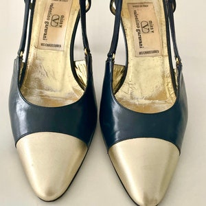 以下が含まれることがあります： 黒と金のポインテッドトゥのヒールシューズのペア。シューズはバックストラップが付いており、インソールには「miss v valentino garavani」のブランド名が印刷されています。シューズはイタリア製です。
