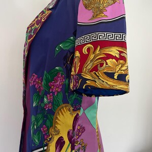 May include: A vintage, knee-length dress in shades of blue, purple, and yellow. The dress features a vibrant floral and ornamental pattern, with gold accents and a Greek key border. The sleeves are short, and the dress has a tailored fit.
