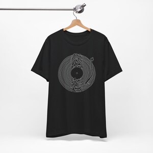 May include: A black short-sleeve t-shirt featuring a white line art graphic on the chest. The design depicts a vinyl record with a tonearm, where the grooves of the record form a mountain-like wave pattern. The shirt is displayed on a wooden hanger.