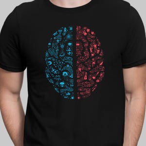 Op de afbeelding: Zwart t-shirt met een hersenafbeelding verdeeld in twee helften. De ene kant is blauw met wetenschappelijke en technologische symbolen, de andere rood met kunst- en muzieksymbolen. De hersenafbeelding staat in het midden.
