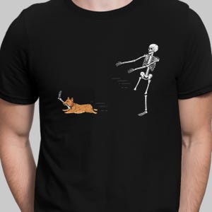 May include: Black t-shirt with a cartoon illustration of a skeleton pursuing a dog. The dog, in shades of brown and orange, runs with a bone. The skeleton and dog are white. A humorous design.