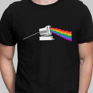 Puede incluir: Una camiseta negra con un gráfico blanco de un monitor de computadora que emite un rayo de luz arcoíris.