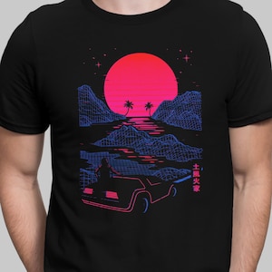 May include: A black t-shirt with a retro-style graphic design featuring a car driving into a sunset landscape with palm trees. The text "土風火祭" is printed on the right side of the design.