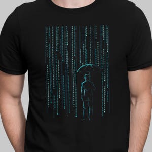 May include: A black t-shirt featuring a graphic of a person holding an umbrella standing in a digital rain of binary code.