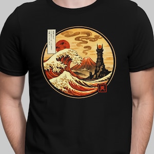 May include: A black t-shirt featuring a circular graphic print. The design depicts a large wave, a mountain, and a dark tower with a glowing eye at the top, set against a warm orange sky with a red sun. Japanese text is visible in a vertical box.