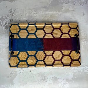 May include: A wooden serving tray with a honeycomb pattern and a blue and burgundy resin inlay. The tray has two black metal handles.