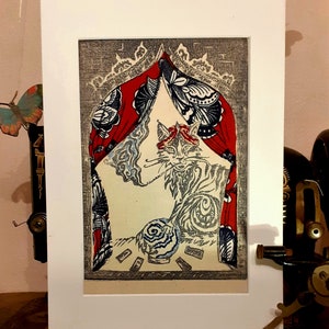 May include: A black and white illustration of a cat sitting under a red and blue patterned canopy. The cat is holding a blue and white orb in its paw. The illustration is framed in a white mat.