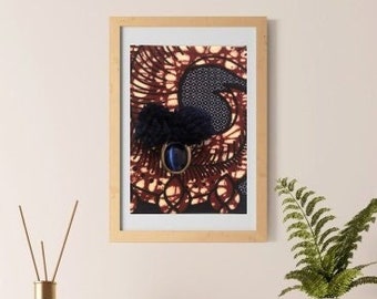 Puede incluir: Una obra de arte enmarcada con un diseño azul oscuro y estampado, un pompón azul oscuro y una gema azul. La obra de arte está en un marco marrón claro. Un jarrón blanco, pequeños jarrones blancos y una caja de madera están sobre una superficie de madera.