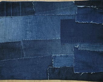 Puede incluir: Un cojín rectangular de patchwork de mezclilla, compuesto por piezas de tela vaquera azul de diferentes tonos, cosidas entre sí. El cojín presenta costuras visibles y bordes sin rematar.