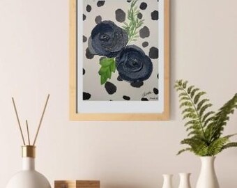 Puede incluir: Pintura enmarcada de rosas azul oscuro con hojas verdes sobre un fondo crema con lunares negros. La obra de arte se exhibe sobre una superficie de madera, con un jarrón blanco y otros objetos decorativos. El marco es de color marrón claro.