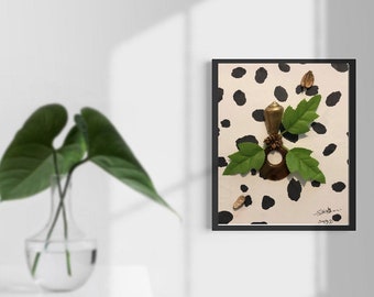 Puede incluir: Una obra de arte enmarcada con un objeto color latón, hojas verdes y un anillo marrón sobre un fondo crema con lunares negros. La obra está encerrada en un marco negro. Probablemente sea una pieza decorativa.