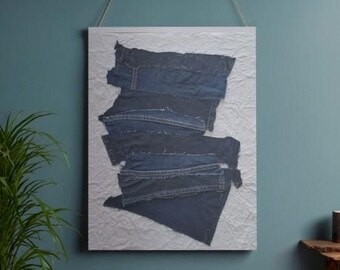 Puede incluir: Arte mural abstracto con piezas de tela vaquera superpuestas en varios tonos de azul. El tejido vaquero está dispuesto sobre un fondo blanco texturizado, creando un diseño único y moderno. La obra de arte está enmarcada y lista para colgar.