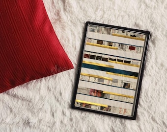 Puede incluir: Una obra de arte enmarcada con un borde negro, con tiras horizontales de periódico, pan de oro y detalles turquesa. Un cojín rojo texturizado descansa sobre una superficie blanca y esponjosa.