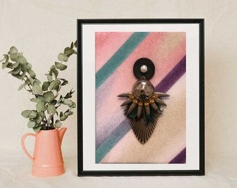 Puede incluir: Obra de arte enmarcada con un colgante decorativo de metal, un disco negro y una cuenta plateada. El fondo tiene rayas diagonales rosas, turquesas y moradas. A la izquierda hay una jarra rosa con vegetación.