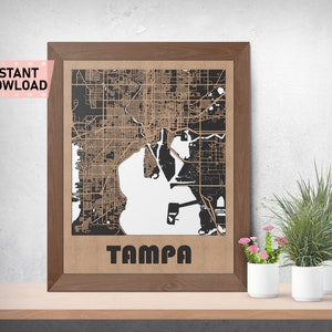May include: A framed map of Tampa, Florida, with a detailed street layout in black and tan. The word "TAMPA" is printed in bold, black letters at the bottom. The frame is a dark wood color, and the words "INSTANT DOWLOAD" are in the upper left corner.
