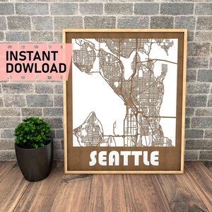 May include: A wood-framed print of a detailed map of Seattle, Washington. The map is laser cut and the city name is printed in white letters at the bottom of the print.