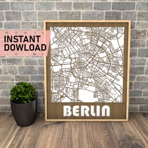 Puede incluir: Un mapa enmarcado de Berlín, Alemania, con un diseño detallado de las calles en color marrón claro. La palabra "BERLIN" se muestra en letras blancas en la parte inferior. Las palabras "INSTANT DOWNLOAD" están en una pancarta rosa en la esquina superior izquierda.