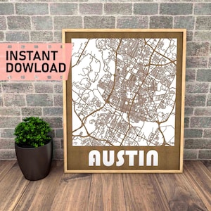 May include: A laser cut wooden map of Austin, Texas, with the city name printed below the map. The map is framed in a light brown wood frame and is displayed against a brick wall.