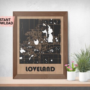 May include: A framed map of Loveland, Colorado, with a black background and white lines depicting the city streets. The city name is printed in brown at the bottom of the map.