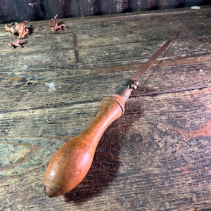 May include: A vintage wooden handled saw with a metal blade. The saw is lying on a wooden surface.