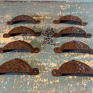 May include: Eight semi-circular metal drawer pulls with a dark brown, textured, rusted finish and embossed floral patterns. Each pull features two screw holes for mounting, and a small pile of matching metal screws is included in the center.
