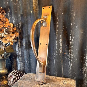 May include: A brass door handle with a curved design. The handle is mounted on a rectangular brass plate.